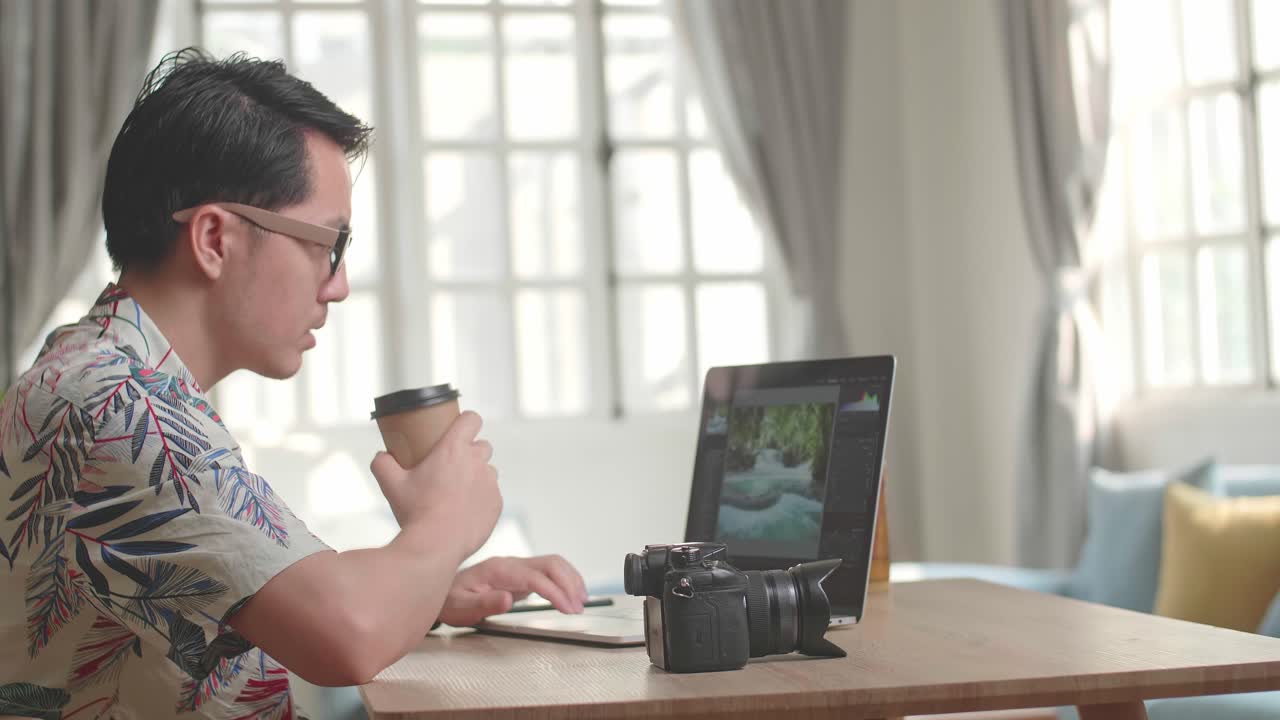 攝影師喝咖啡並在他的手提電腦上使用照片編輯應用程式/軟件工作。照片編輯師修飾美麗的自然風景照片。