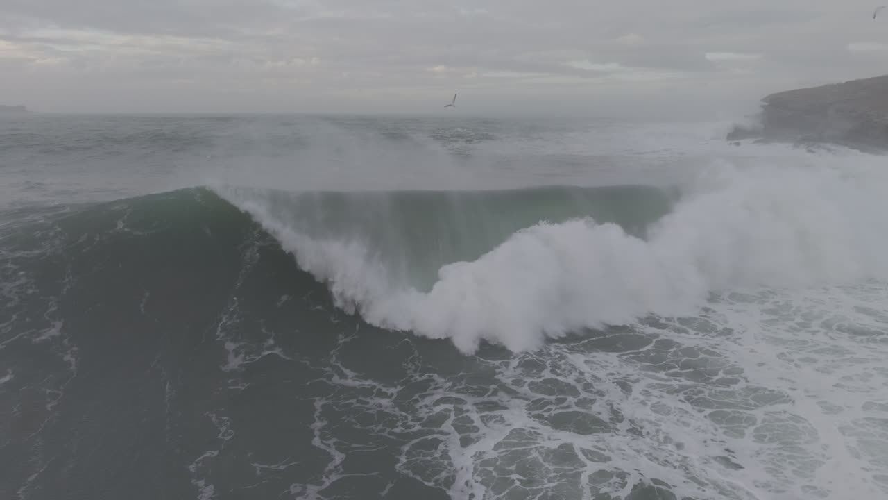 Powerful Ocean Wave Breaking Near Rocky Coastline on Overcast Day