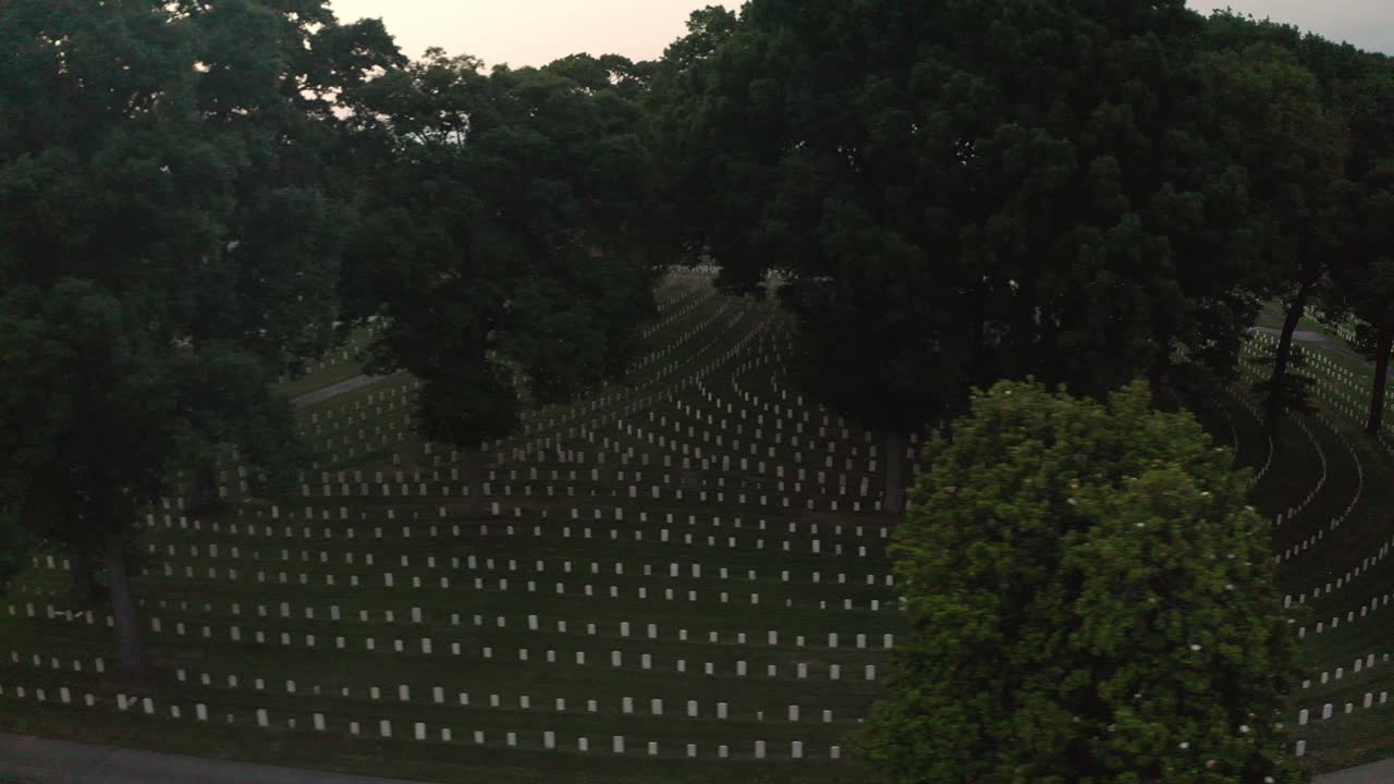 Aerial view of rows of white gravestones in a vast national cemetery with trees and pathways