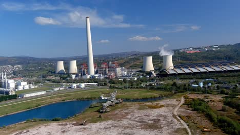 Planta-De-Energía-Térmica-Con-Chimenea-Humeante,-Lago-En-Frente-Con-Una-Vieja-Máquina-De-Excavación,-Tarde-Brillante-Y-Soleada