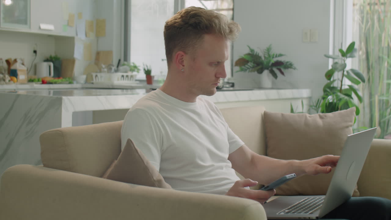 Young Man Using Laptop and Smartphone at Home