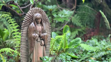 Primer-Plano-De-Una-Escultura-Virgen-De-Estilo-Mexicano-Con-Vegetación-Selvática-Verde-En-El-Fondo-Durante-La-Temporada-De-Lluvias