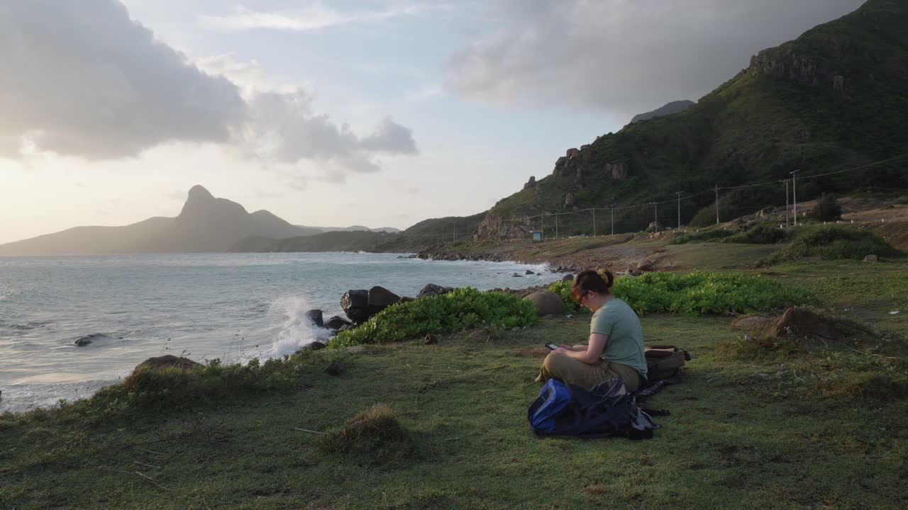 donna caucasica seduta sulla riva del mare che legge un libro su un dispositivo kindle nell'isola di con dao, in vietnam