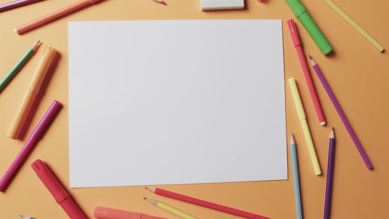 vista aérea de una hoja en blanco de papel con papelería escolar sobre un fondo beige, en cámara lenta