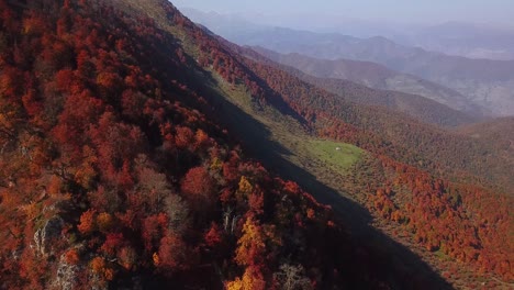 Schönste-Drohnenaufnahme-Auf-Dem-Hyrkanischen-Wald-In-Der-Herbstsaison.-Bäume-Mit-Buntem-Laub-Auf-Bergfelsen-Und-Sonnenuntergangsschatten-Auf-Grünen-Wiesen-Und-Berglandschaften-Im-Dunstigen-Tagesblau-Im-Iran