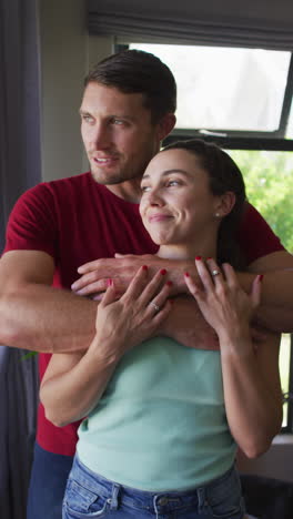 video vertical de una feliz pareja caucásica abrazándose y mirando por la ventana