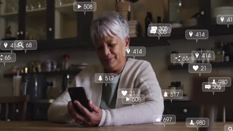 Animación-De-íconos-De-Redes-Sociales-Y-Números-En-Pancartas-Sobre-Una-Mujer-Mayor-Usando-Un-Teléfono-Inteligente