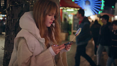 una mujer de moda enviando mensajes de texto con un teléfono inteligente sosteniendo una piruleta en un primer plano festivo de la calle.
