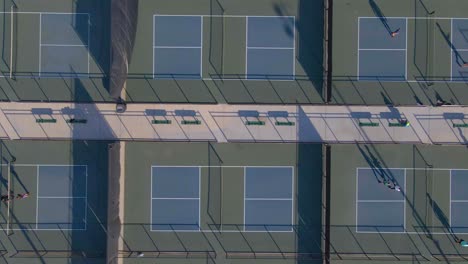 gente jugando y caminando dentro de las canchas de pickleball con bancos en medio en un día soleado