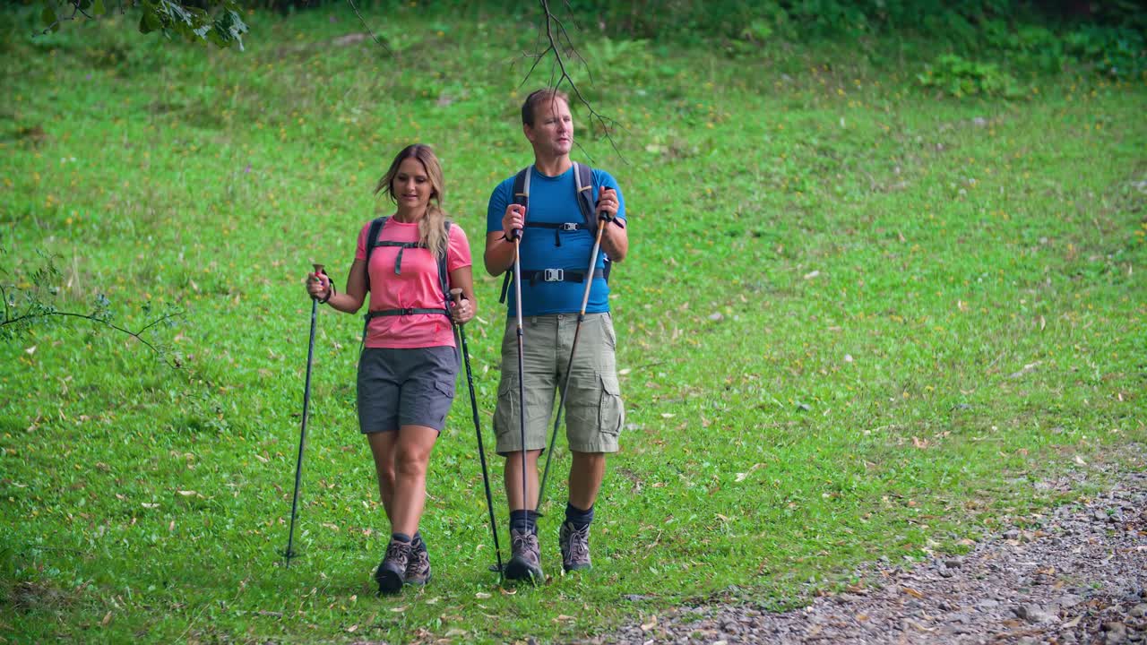 Slow motion of an active couple hiking with poles in a forest and looking in the distance