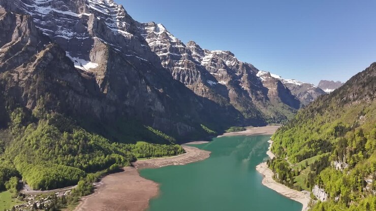 Le acque turchesi del lago Klöntalersee serpeggiano attraverso una valle incorniciata da montagne scoscese e innevate in Svizzera. Un concetto di serenità alpina incontaminata.