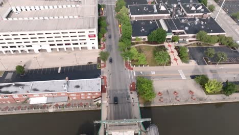 Traffic-driving-over-a-bridge-over-Des-Plaines-River-in-Joliet,-Illinois-with-drone-video-tilting-up-from-bridge-to-skyline