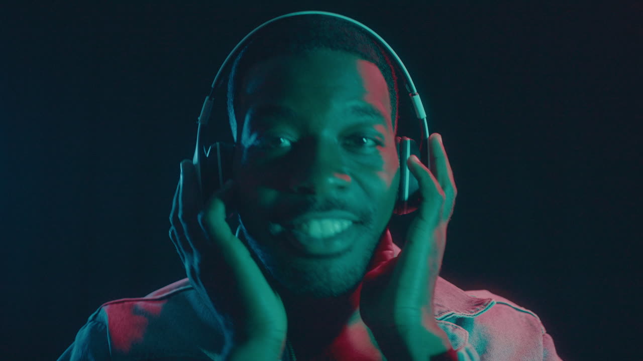 Happy Black Man in Headphones Dancing Under Colorful Neon Lights