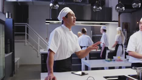 Mixed-race-male-chef-wearing-chefs-whites-in-a-restaurant-kitchen,-using-a-tablet