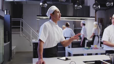 cocinero de raza mixta vestido con ropa blanca en una cocina de un restaurante, usando una tableta
