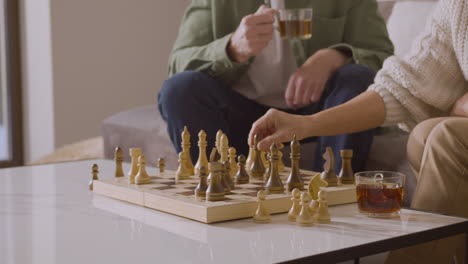 älterer mann und frau, die schach spielen und tee trinken, während sie zu hause auf dem sofa sitzen 1