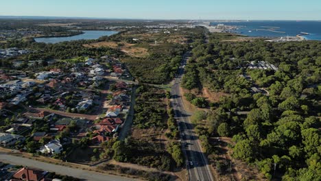 Vista-Panorámica-Aérea-Del-Tráfico-En-La-Carretera-Principal-En-El-Suburbio-De-La-Ciudad-De-Perth-Y-El-Puerto-En-Segundo-Plano,-Australia-Occidental