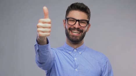 retrato de un hombre feliz con gafas que muestra los pulgares hacia arriba. visión, gafas y concepto de personas <unk> retrato de video de un joven feliz y sonriente con barba en gafas que mostra los pulgaros hacia arriba sobre un fondo gris