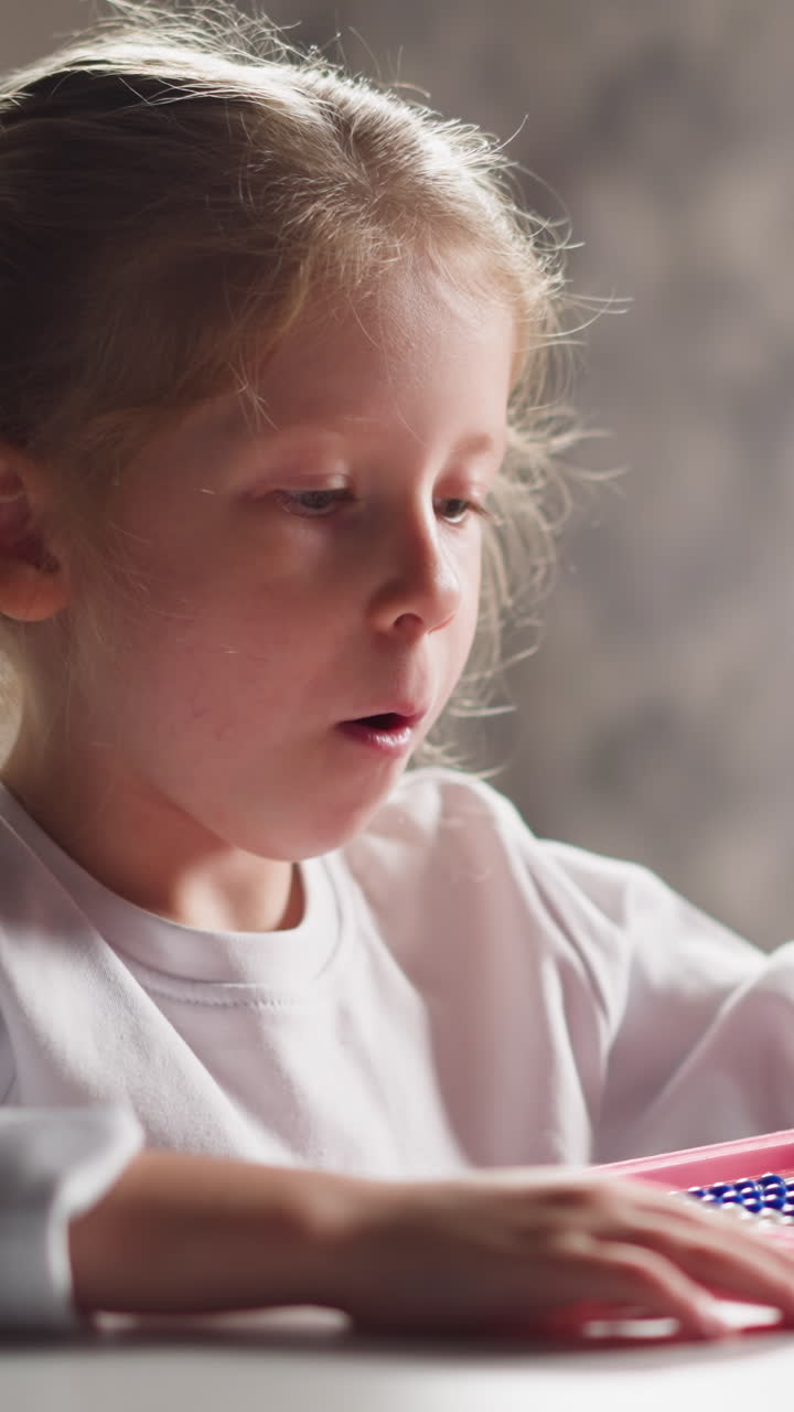 Inspired little blonde girl learns to count with colorful traditional toy abacus sitting at desk at mental arithmetics lesson closeup slow motion