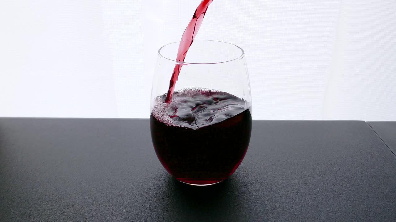 Vino rosso Bordeaux versato nel bicchiere da vino su sfondo bianco