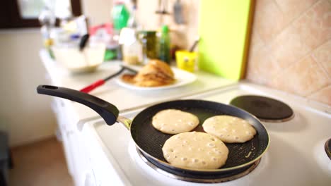 three pancakes are fried in a frying pan, on an electric stove, against the background of the kitchen table.