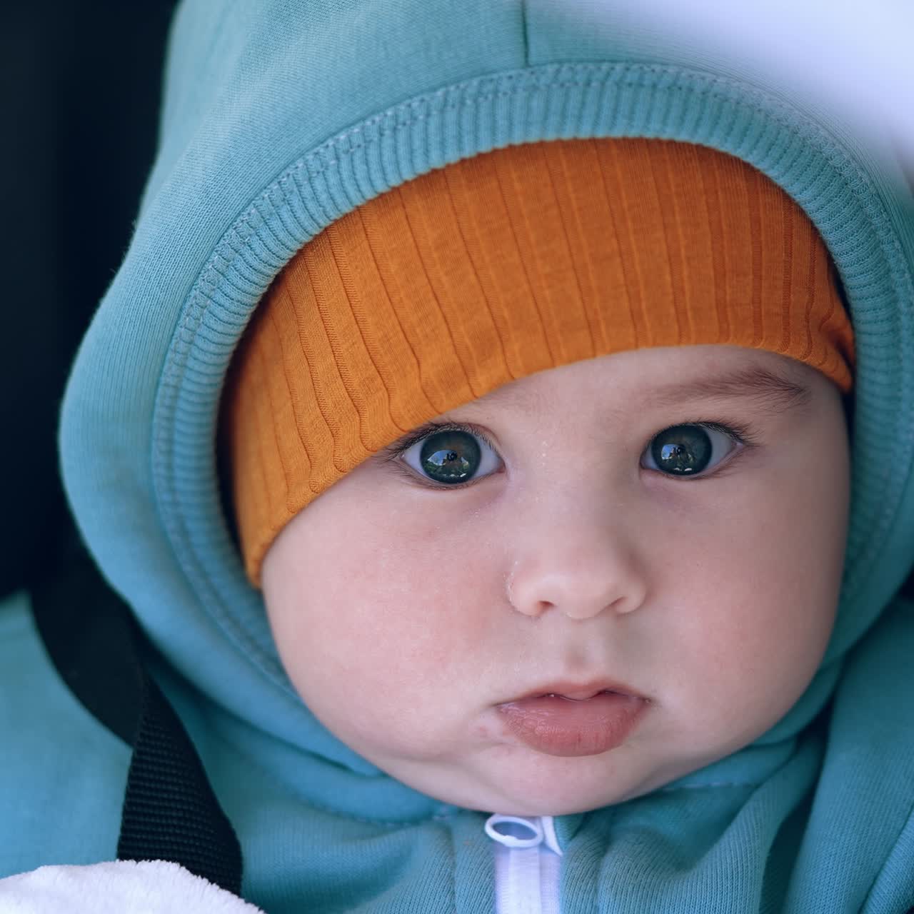 Funny beautiful baby boy in blue blazer and yellow cap. Cute toddler sitting in stroller looks into camera with surprise