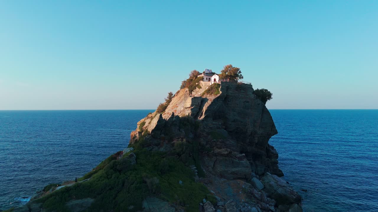 해가 지는 동안 푸른 바다 한가운데에 있는 바위 섬, 꼭대기에 나무가 있습니다.