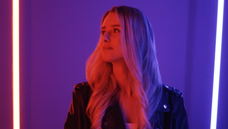 Close-Up-View-Of-Blonde-Young-Woman-Standing-Among-Neon-Lights-And-Smiling-Cheerfully-To-The-Camera-1