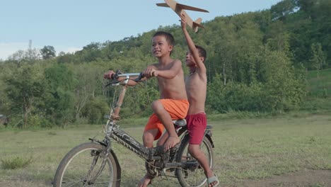 two boys riding a bicycle and playing with a paper airplane