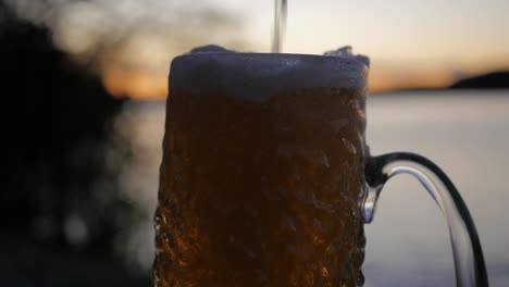 mientras el sol se pone en el archipiélago sueco, se vierte una cerveza lager fría en un vaso de cerveza ondulado en cámara lenta