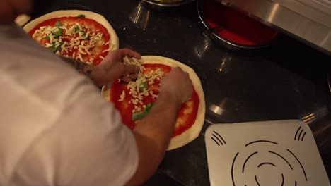 professional cook adding fresh cheese pieces on the pizza dough covered in tomato sauce and basil leaves in restaurant kitchen. pizza preparation in restaurant