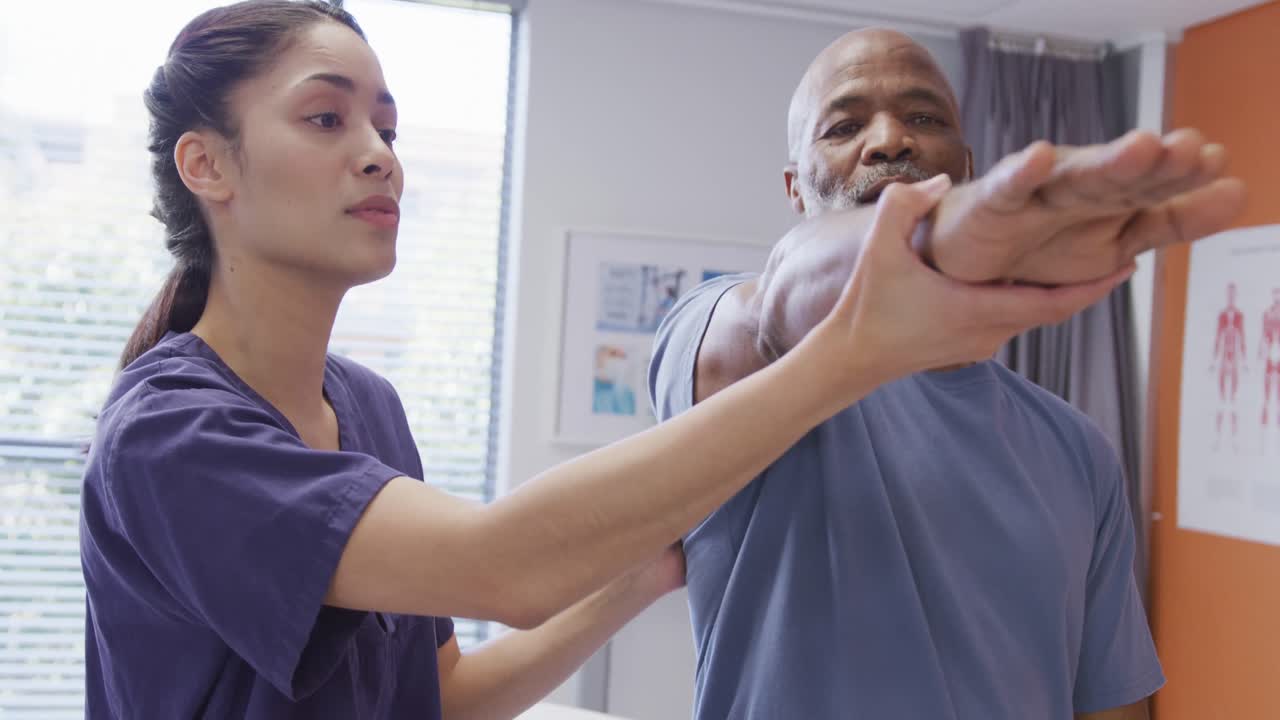 Diverse female physiotherapist and senior male patient working on arm in physical therapy