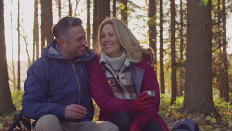 loving mature couple stop for rest and hot drink on walk through fall or winter countryside - shot in slow motion