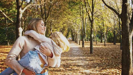 young mother is smiling, holding little daughter in her arms and circling around during their walk in autumn park