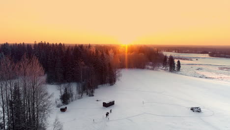 Aerial-view-showing-family-walking-on-snowy-winter-path-in-forest-during-golden-sunset-at-horizon