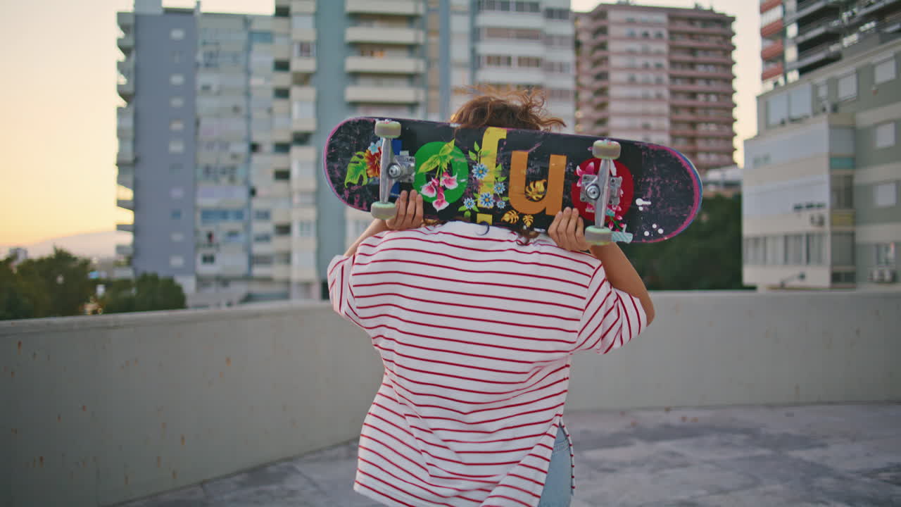 chica patinadora llevando una patineta caminando por el techo de un edificio. patinador relajándose