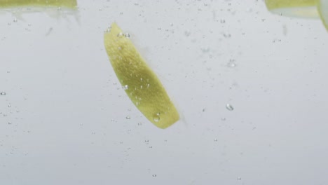 video of slices of lime and lemon falling into water with copy space on white background