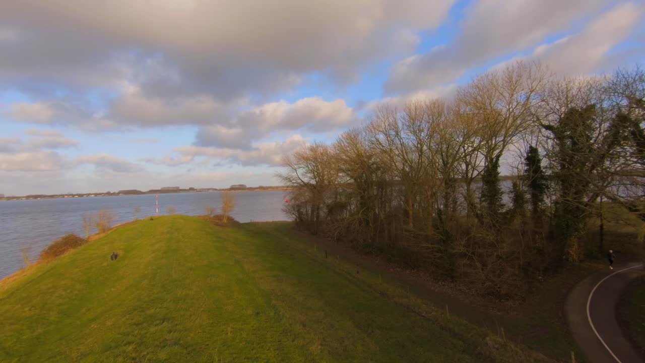 Drone shot of a bike path with jogger going through a forest next to a lake