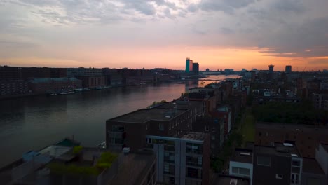 Fliegen-über-Die-Skyline-Von-Amsterdam-Bei-Sonnenuntergang-Per-Drohne-über-Den-Ij-Fluss-In-Der-Nähe-Des-Hauptbahnhofs-Mit-Wunderschönem-Roten-Himmel-Und-Weißem-Zug-In-Richtung-Zum-Bahnhof