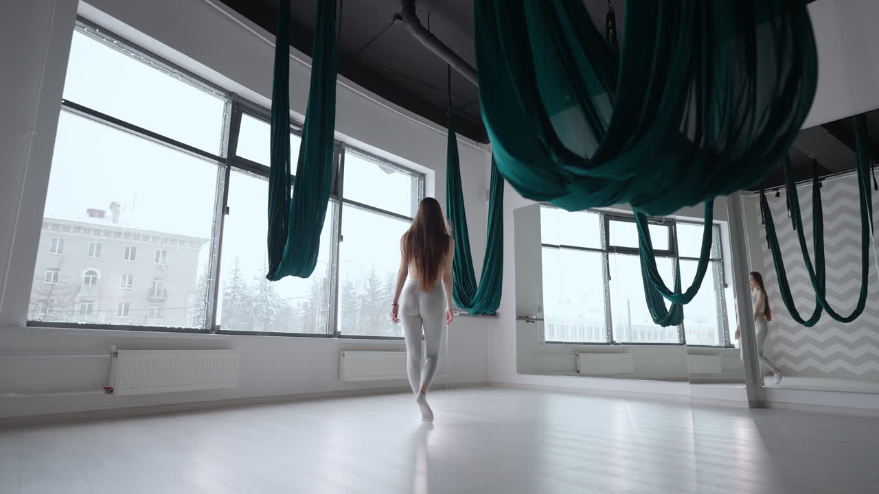 una mujer joven en cámara lenta se prepara para comenzar una clase de estiramiento y yoga en una hamaca. enderezar el tejido de la hamaca en desarrollo antes del entrenamiento