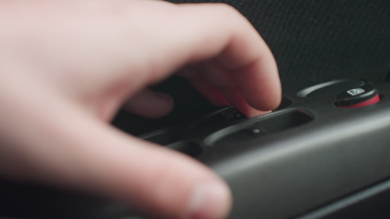close up of fair skinned hand pressing then lifting finger from auto window switch on car door panel showing plastic button detail red accent fabric trim texture under natural light interior scene
