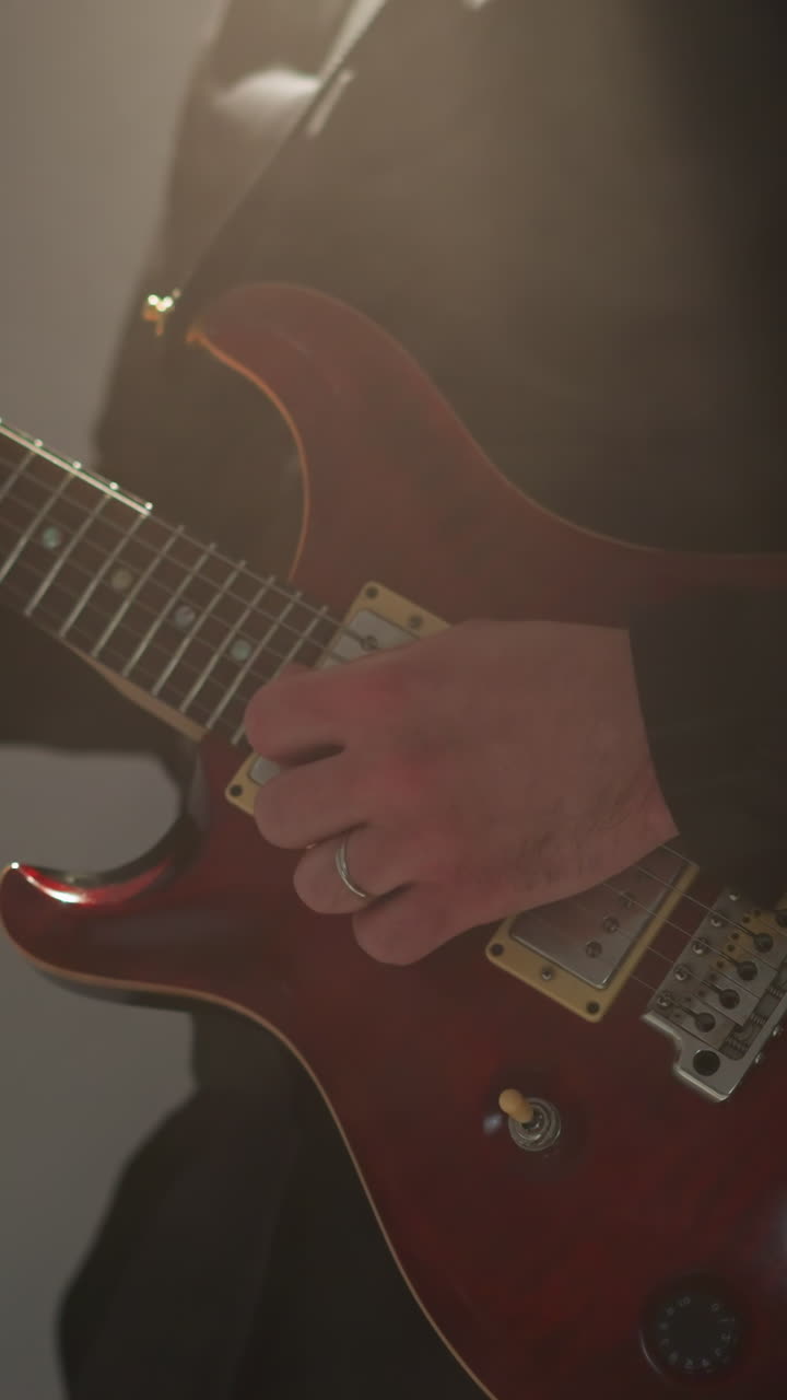 Close-up of a faceless person in black playing a red guitar in a dimly lit room