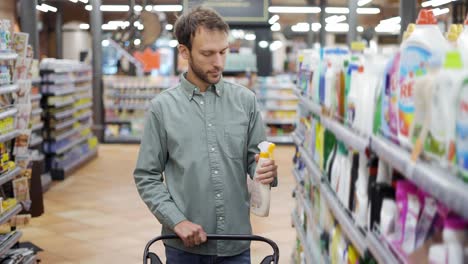 man walks through the supermarket and takes goods from the shelf in household chemicals department