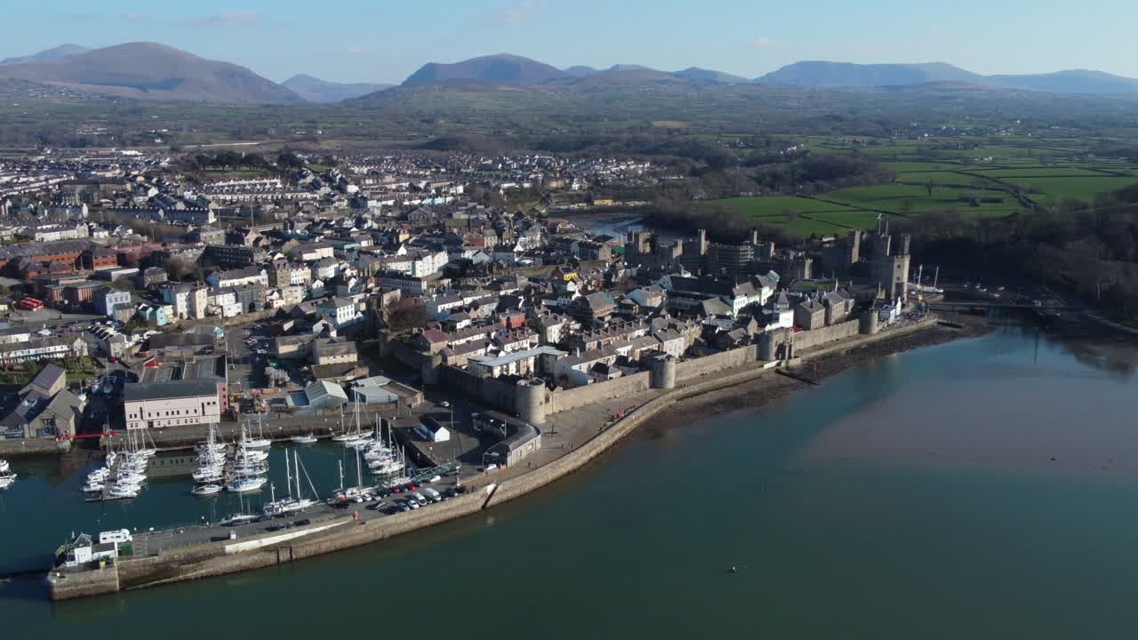 una vista aérea de la ciudad de caernarfon en un día soleado, volando de izquierda a derecha sobre el paseo marítimo y la zona del puerto, gwynedd, gales del norte, reino unido