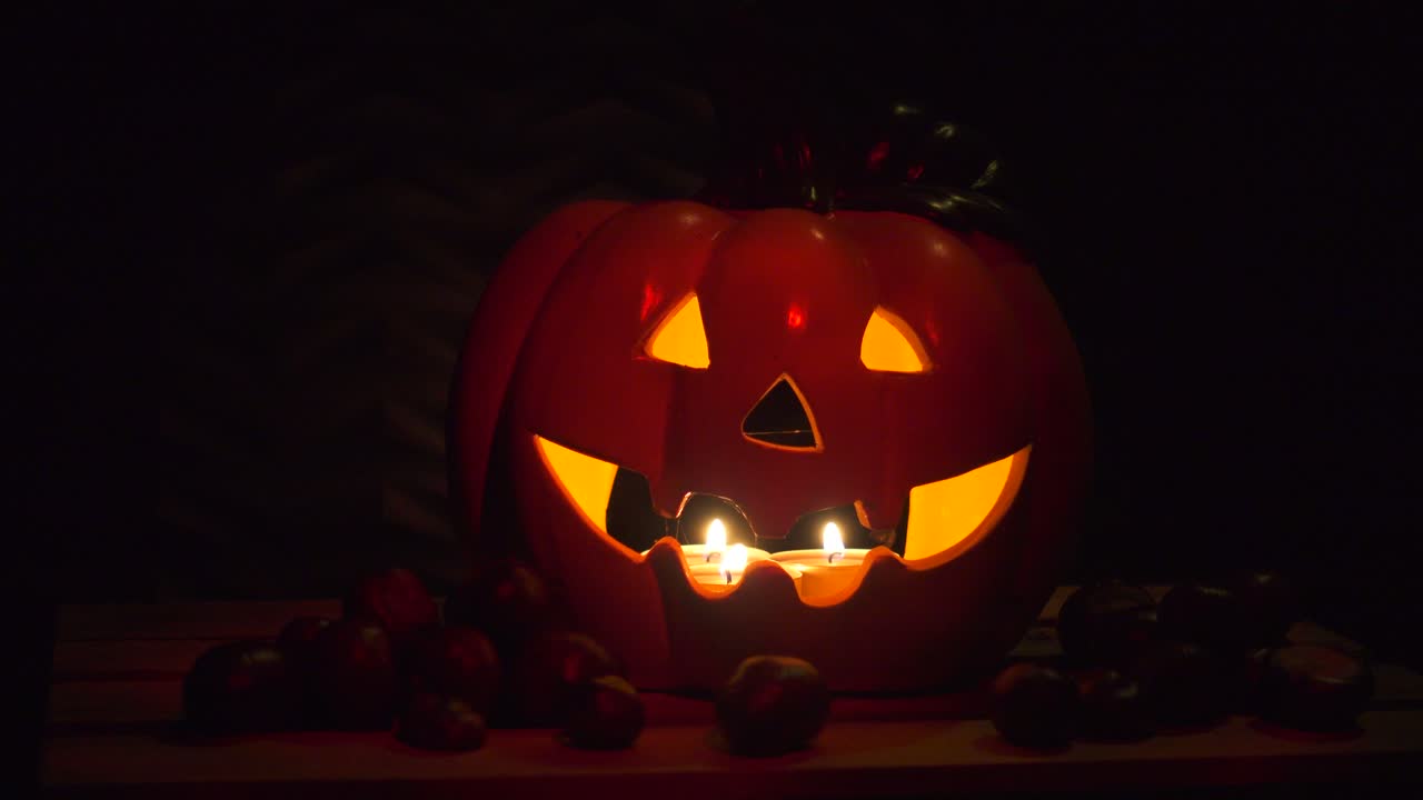 calabaza de halloween de fondo oscuro con castañas, iluminada por velas, resplandor rojo oscuro sobre negro, aislada con espacio de copia, concepto de vacaciones, decoración, pan de izquierda a derecha, paralaje