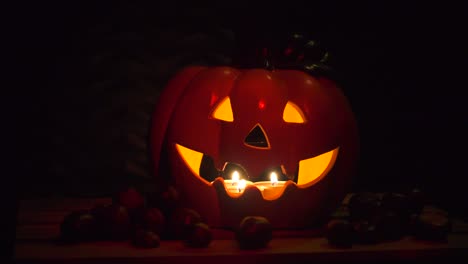 halloween pumpkin od dark background with chestnuts, illuminated by candles, dark red glow on black, isolated with copyspace, holiday concept, decoration, pan left to right, parallax