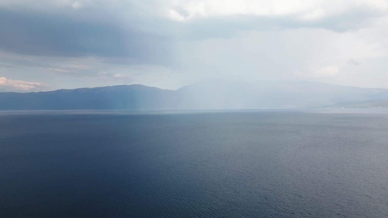 Aerial drone view of Lake Ohrid in Albania under a cloudy sky with calm blue water and distant mountains. Peaceful and scenic natural landscape