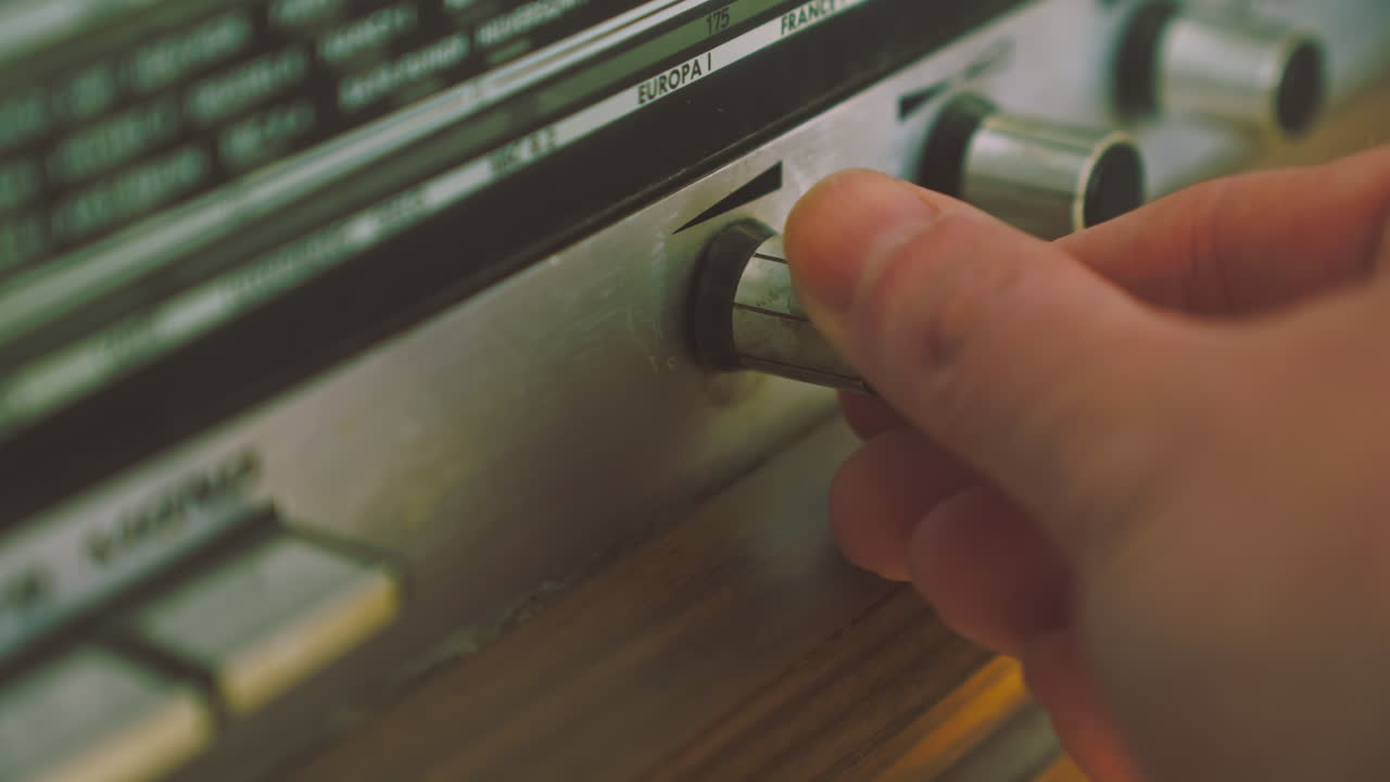 Close view of fingers rotating volume knob on retro radiogram audio system. Suitable for analog sound control, vintage electronics and broadcasting visuals