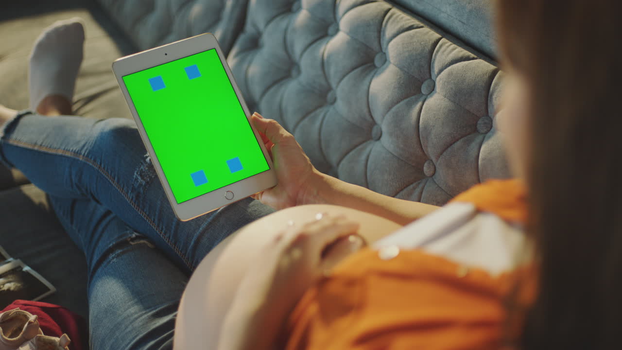 Pregnant woman using a tablet on a couch.