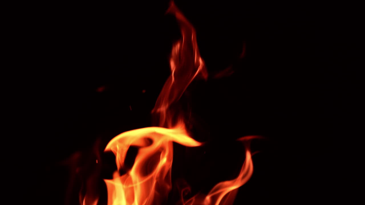 Dancing fire flames in total darkness. Tongues of blaze swaying to and fro and tiny sparkles flaring at night.